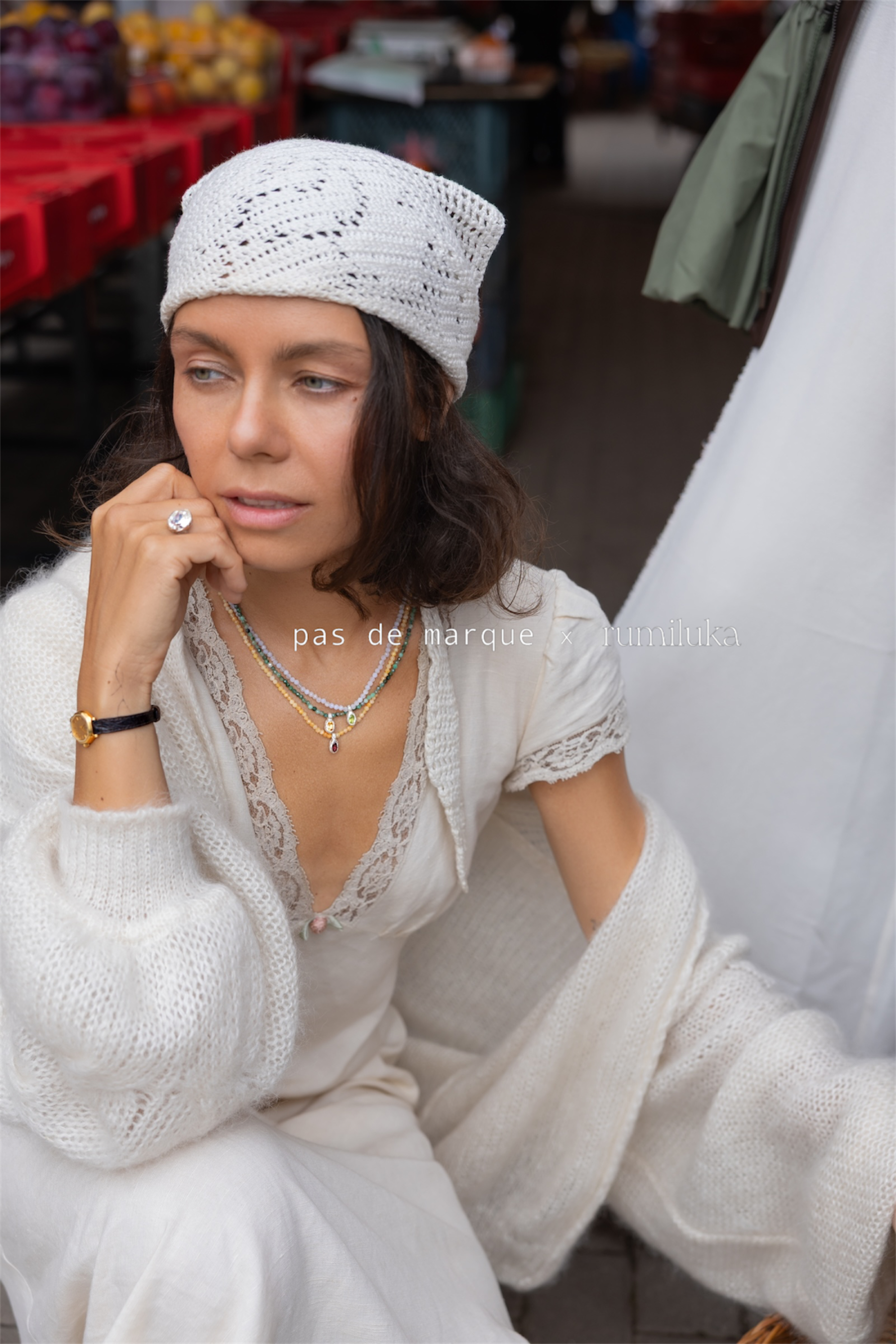 A woman wearing a cream-colored knit beanie, a matching lace-trimmed knit top, and a chunky knit cardigan, posing in a market setting. A watermark reading 'pas de marque - thimistral' is visible across the center.
